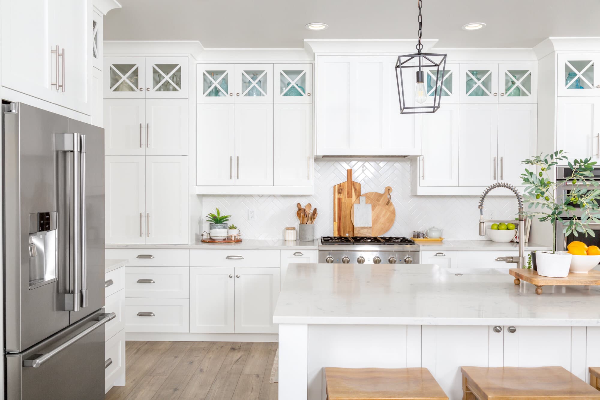 A bright white kitchen with white countertops, stainless steel fridge, and white cabinets.