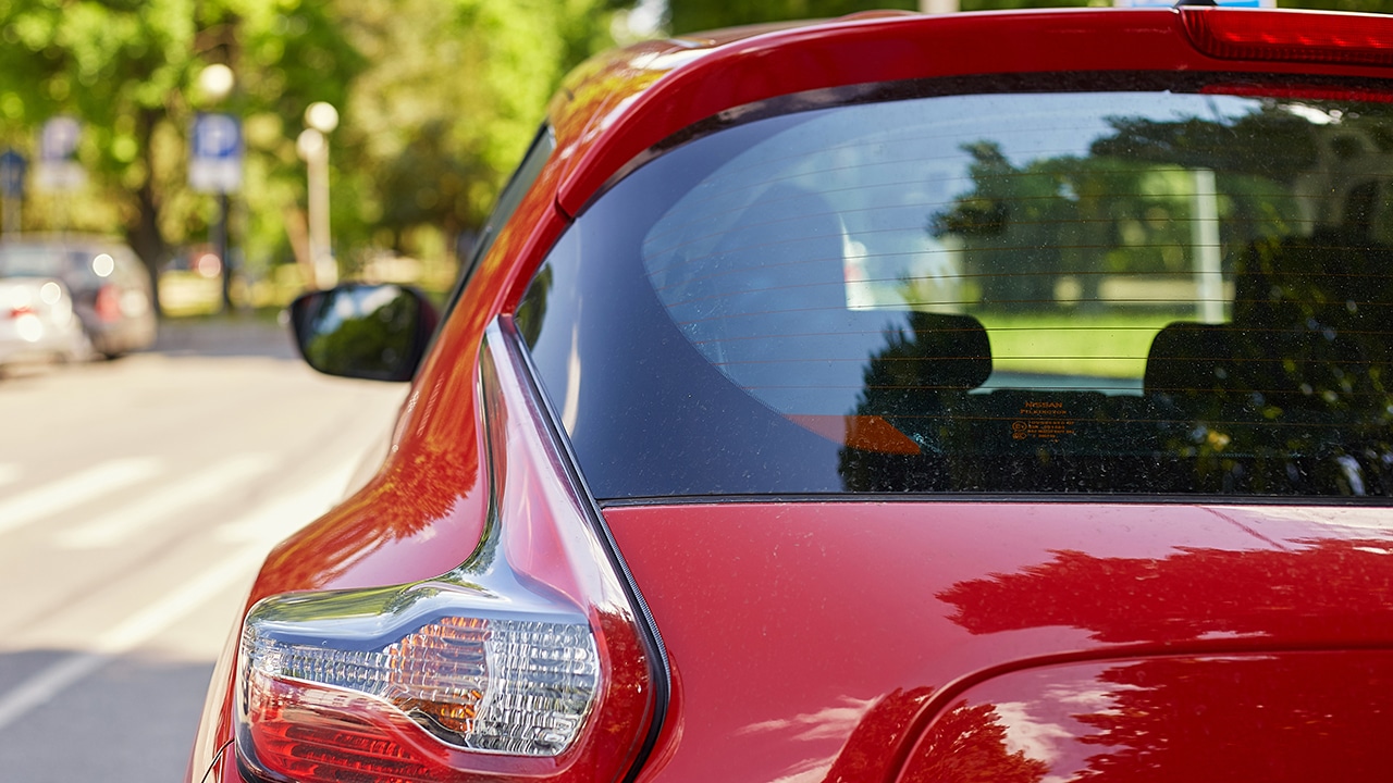 Back window of red car parked on the street in summer sunny day, rear view.