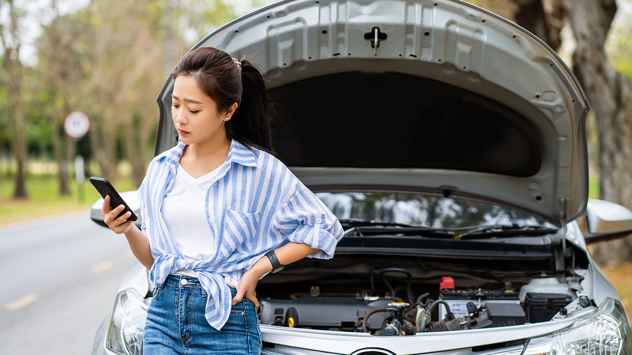 Beautiful asian woman sitting on a car broke down on the road.