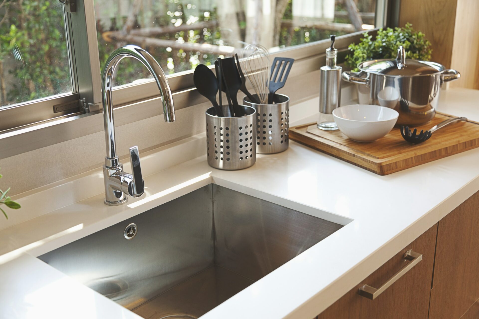 Stainless steel kitchen sink with woodgrain cabinets and white marble countertops.