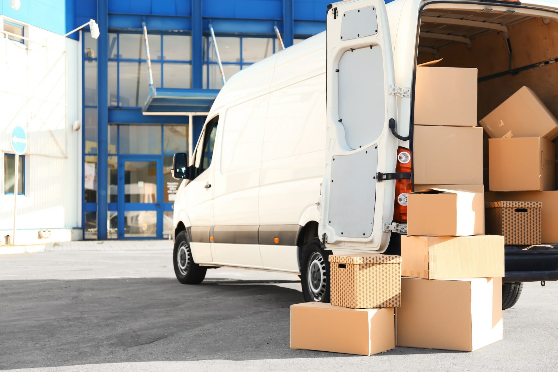 White van with open trunk surrounded by moving boxes outdoors.