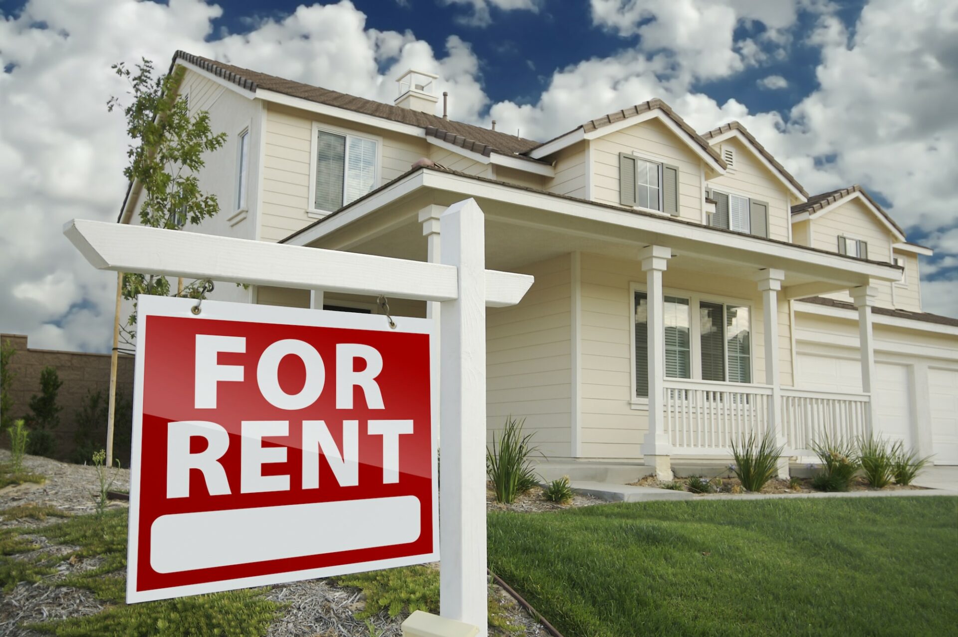 Red "For Rent" real estate sign in front of a beautiful cream colored house.