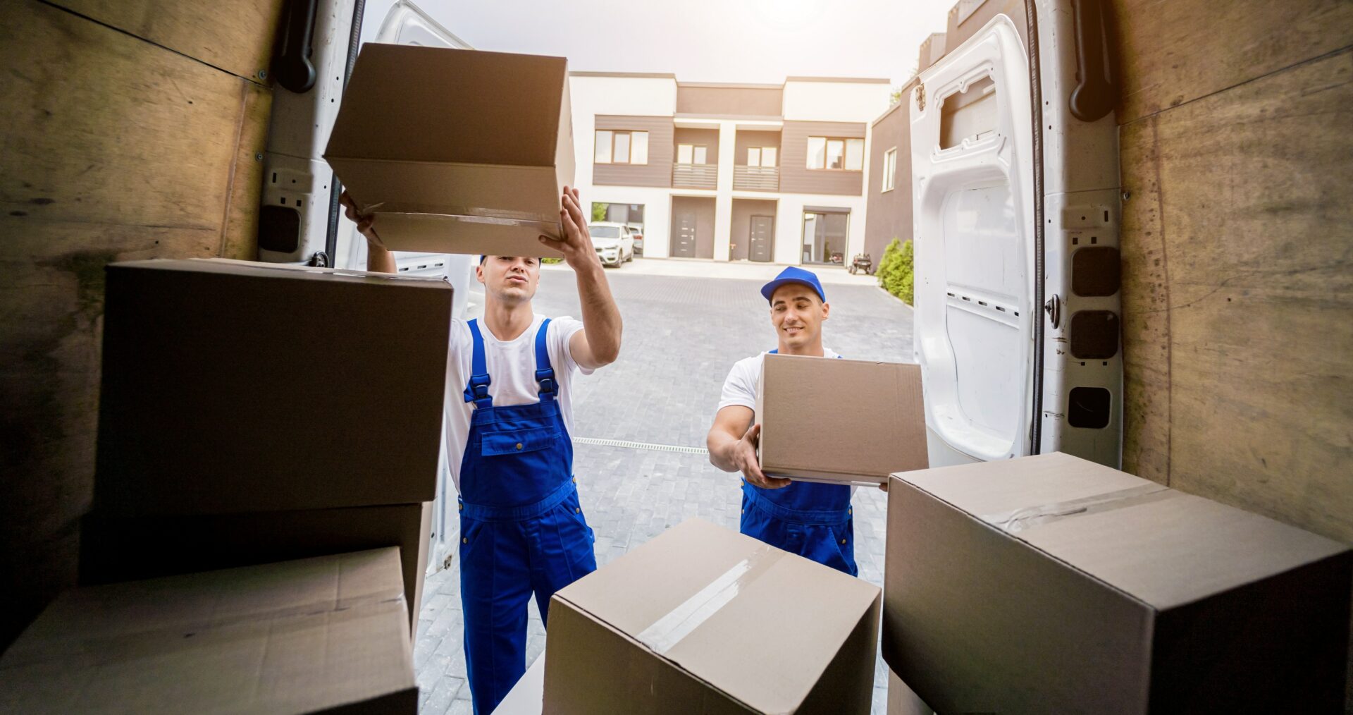 Two moving company workers unloading boxes from minibus.