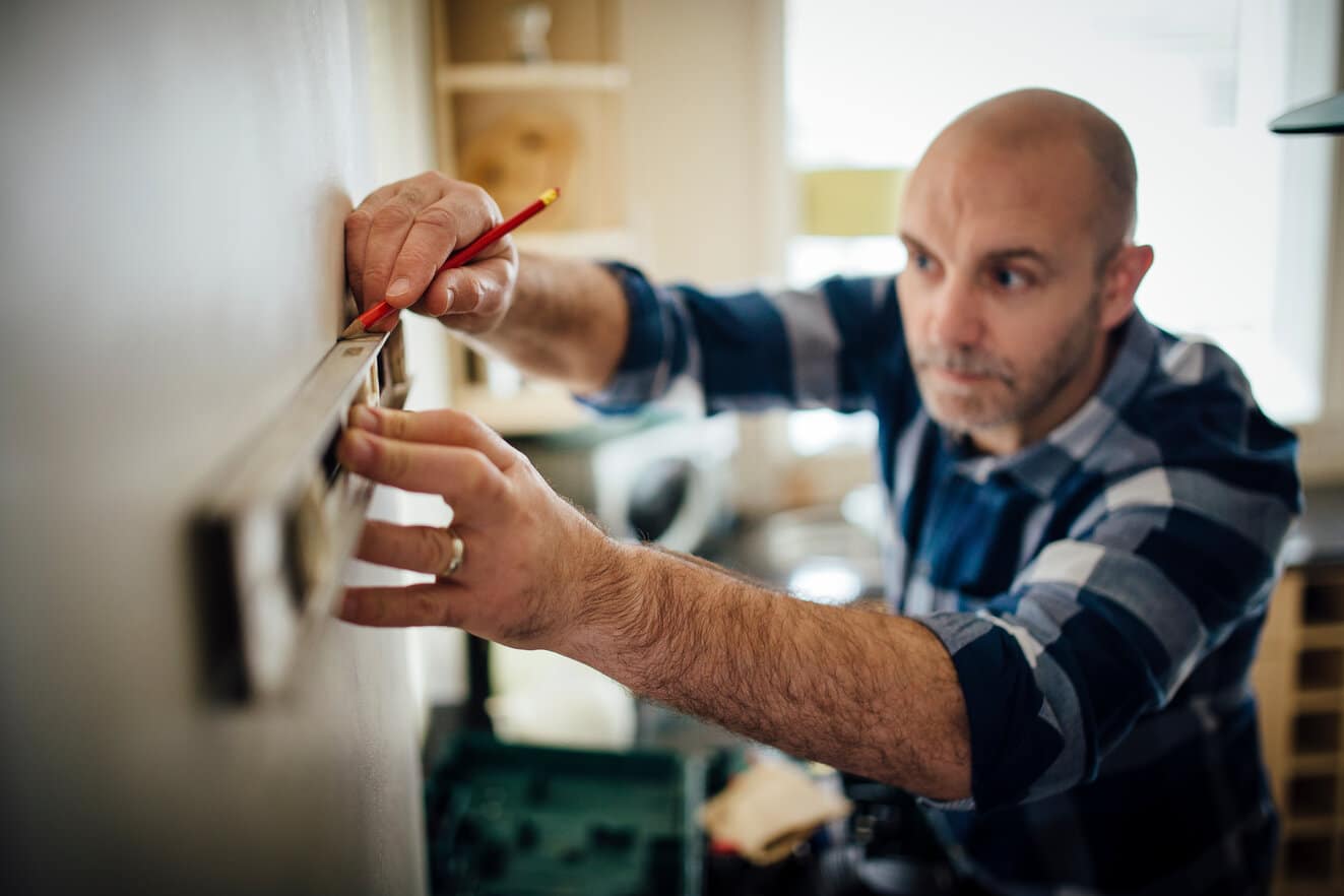 A man holds a level against the wall while working on a home DIY project