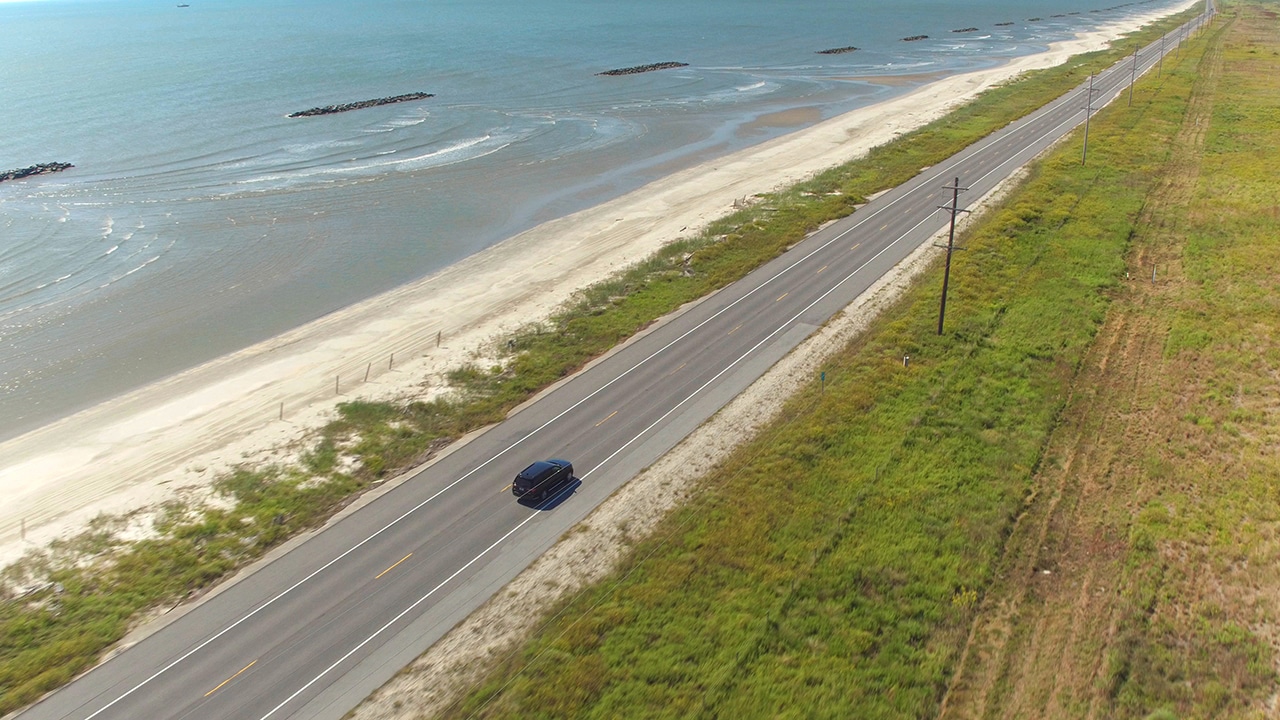 Black SUV car driving on countryside road. People traveling, road trip on empty road through beautiful countryside scenery in sunny summer