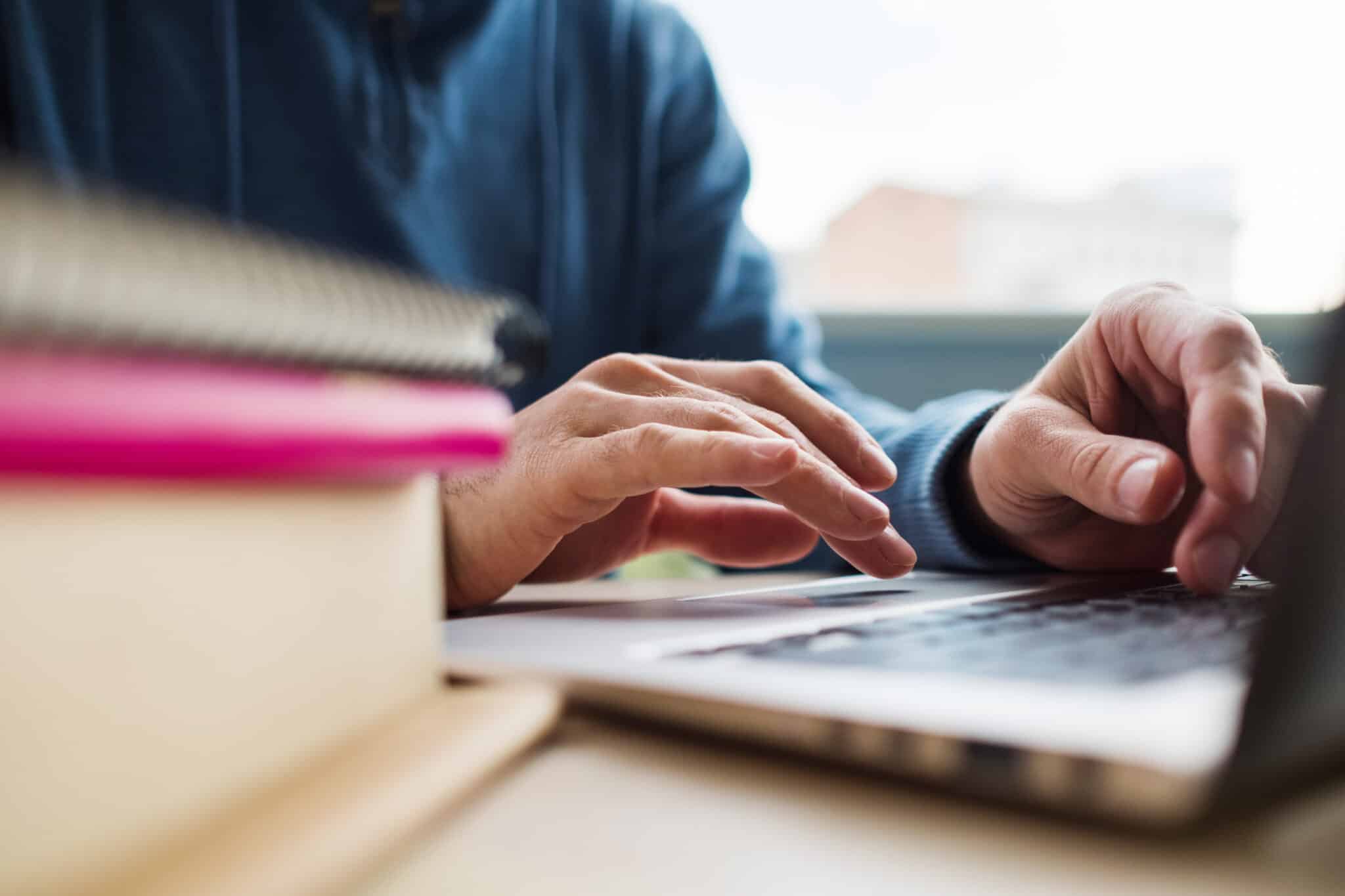 view of hands in long shirt typing on laptop keys with books in foreground learning how to file for divorce online