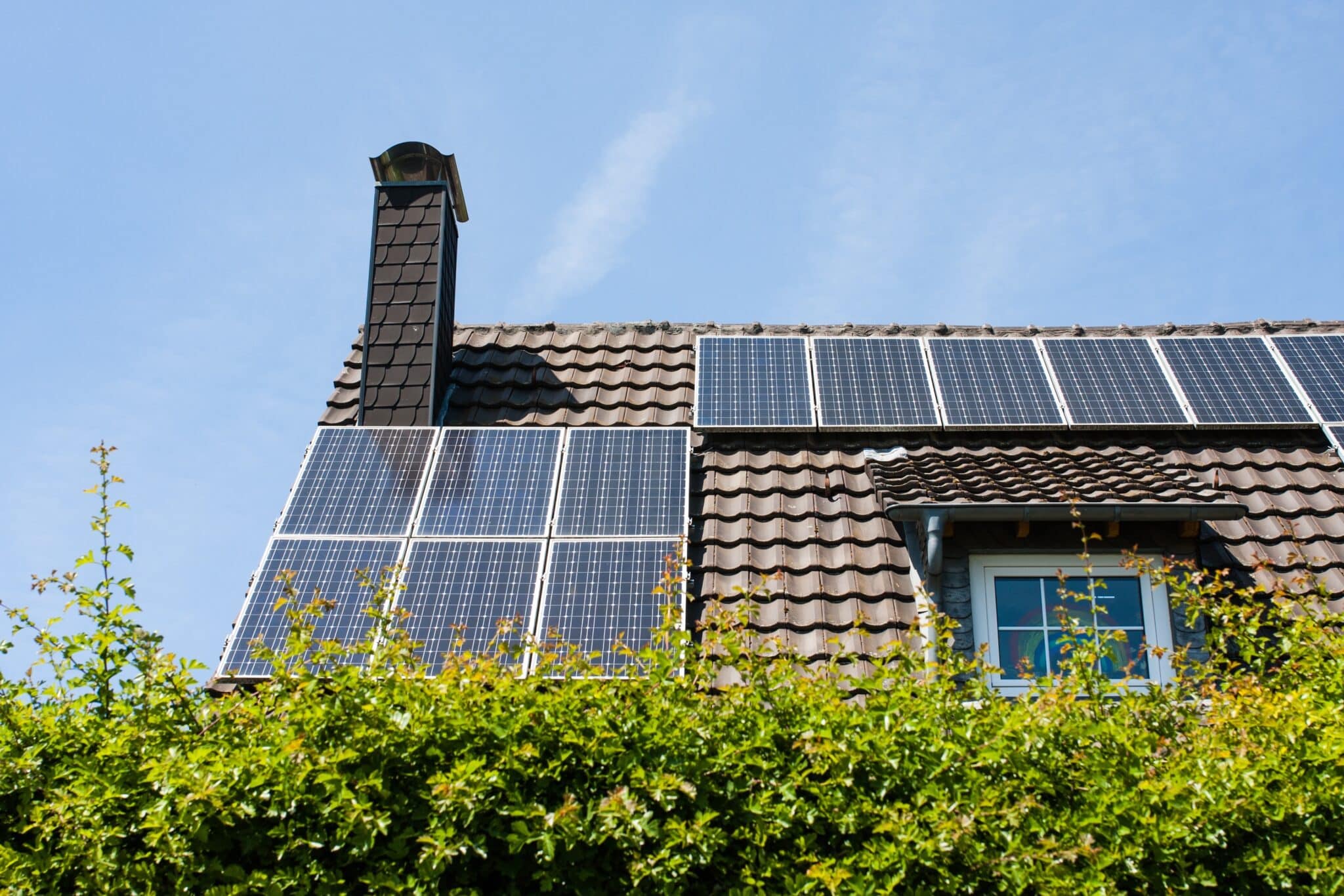 A home with chimney and brown roof with black rectangular solar panels