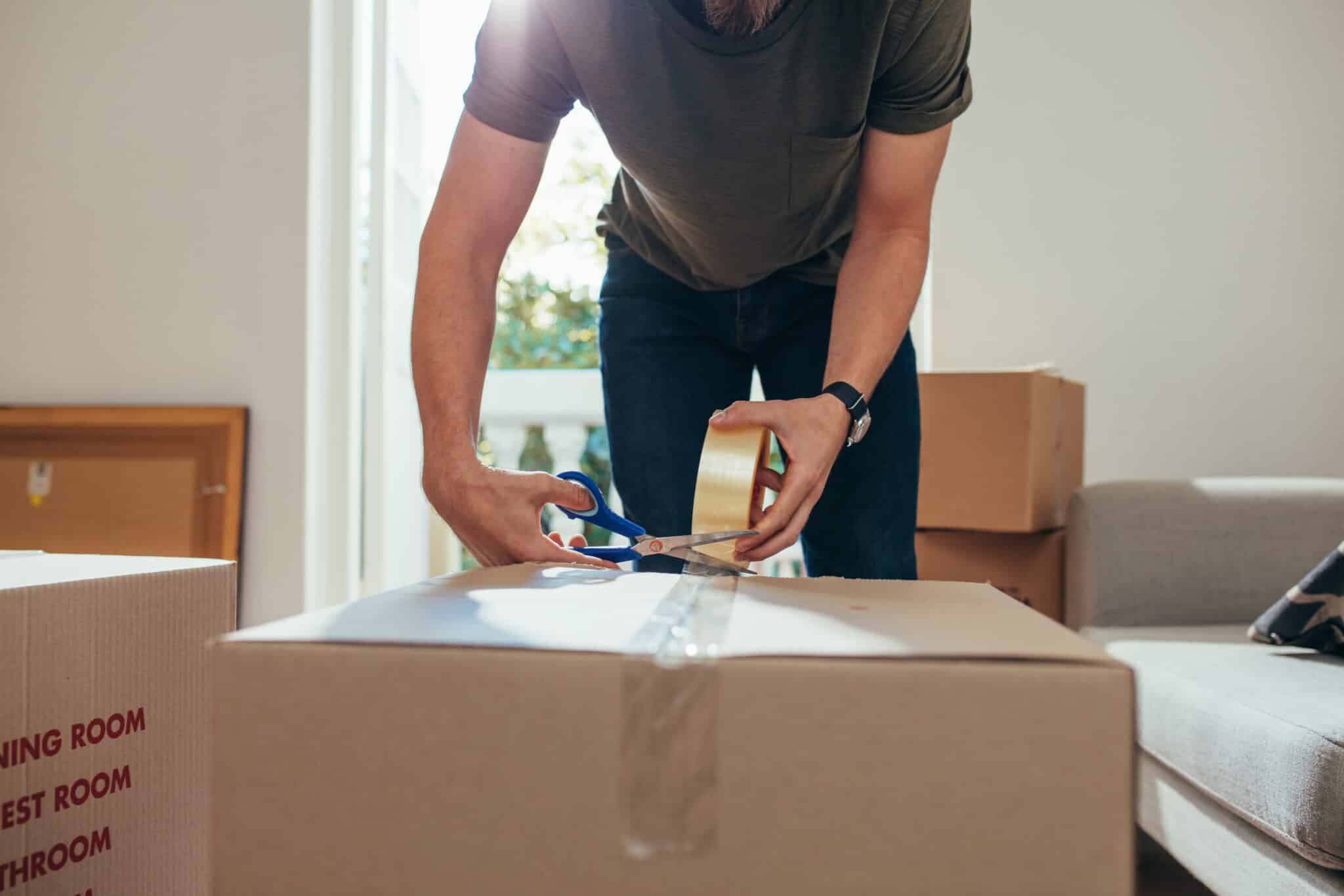 Close up of a man applying adhesive tape on a packing box. Man cutting adhesive tap using scissors after sealing the box.