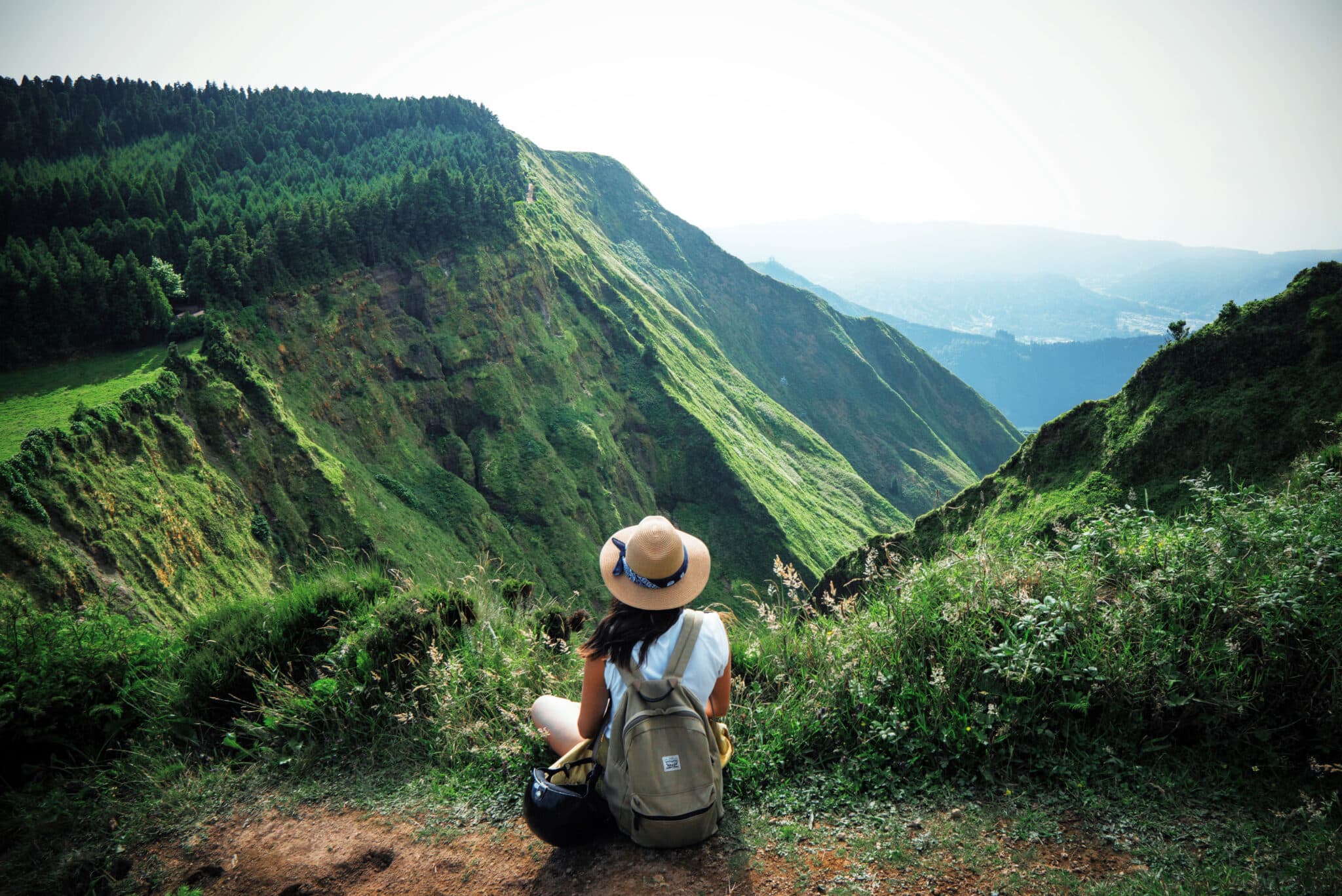 woman traveler holding hat and looking at amazing mountains and forest, wanderlust travel concept, space for text, atmospheric epic moment, azores ,portuhal, ponta delgada, sao miguel