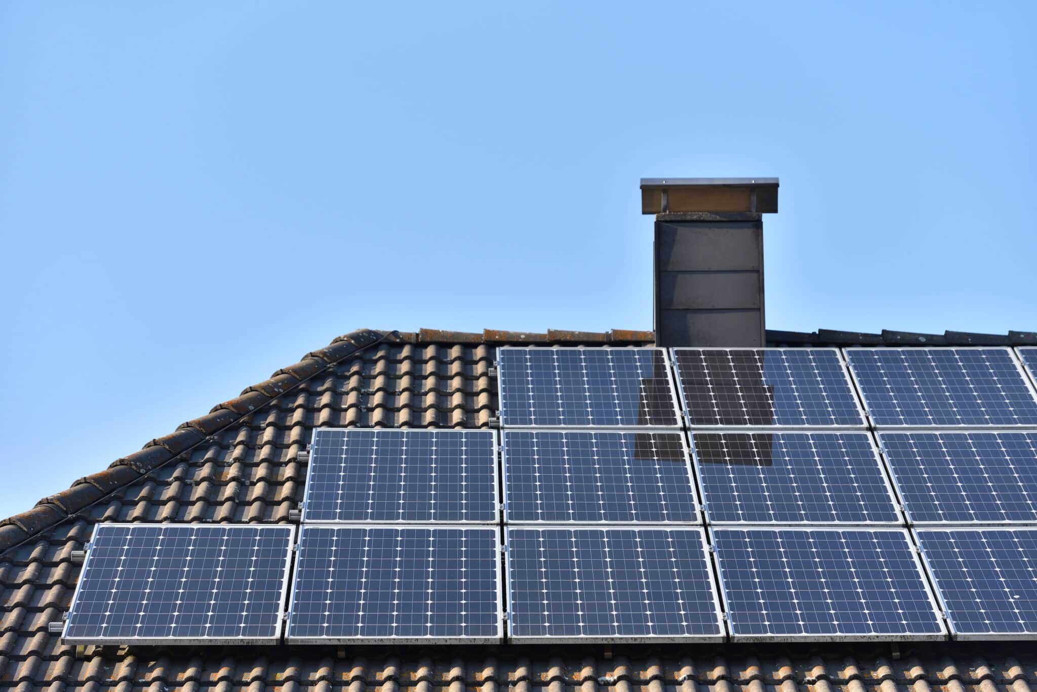 Solar panels installed on the roof of a house with tiles in Europe against the background of a blue sky.