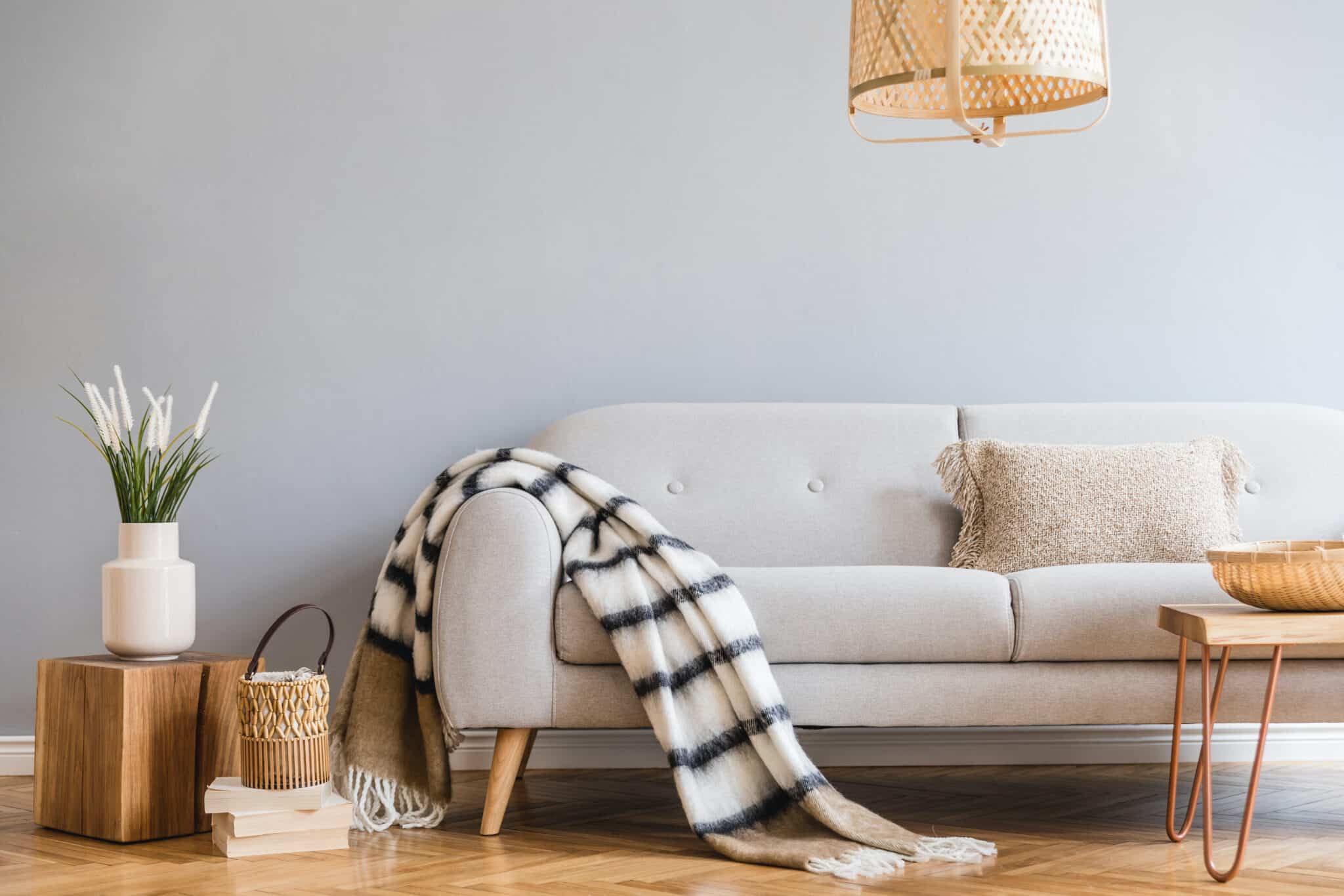 Stylish and design home interior of living room with gray sofa, wooden coffee table , pillows, blankets, rattan lamp, cube flowers, basket and elegant accessories. Stylish home decor. Template.