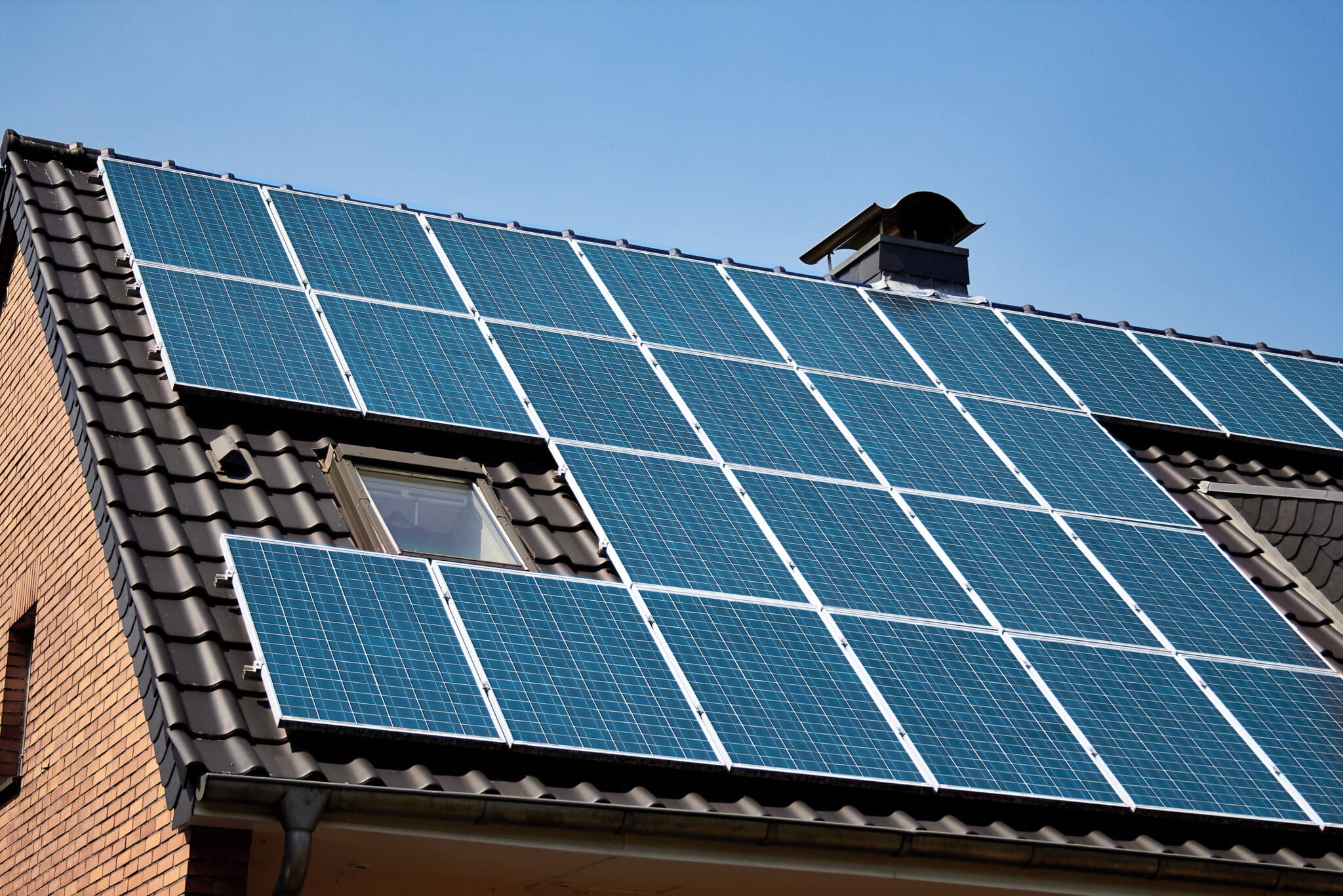 Part of installed on a rooftop sun panel system. Roof surface covered with sun collectors. Brick house equipped with solar panels to power a houshold. Solar energy for generating electricity.