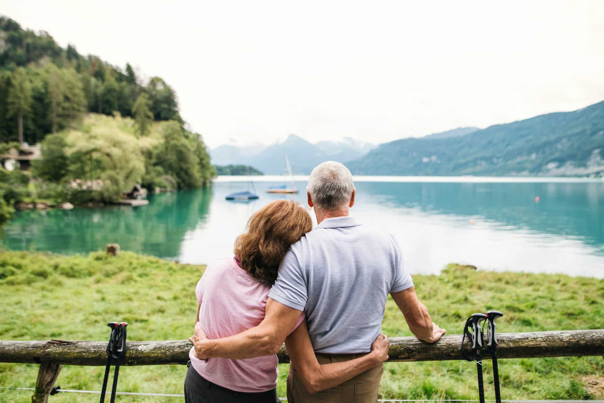 A rear view of senior pensioner couple standing by lake in nature. Copy space.