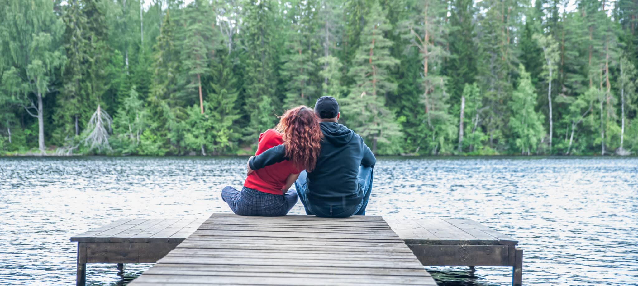 Guy and a girl sit hugging on the pier of a beautiful lake. The concept of love, the summer mood , banner