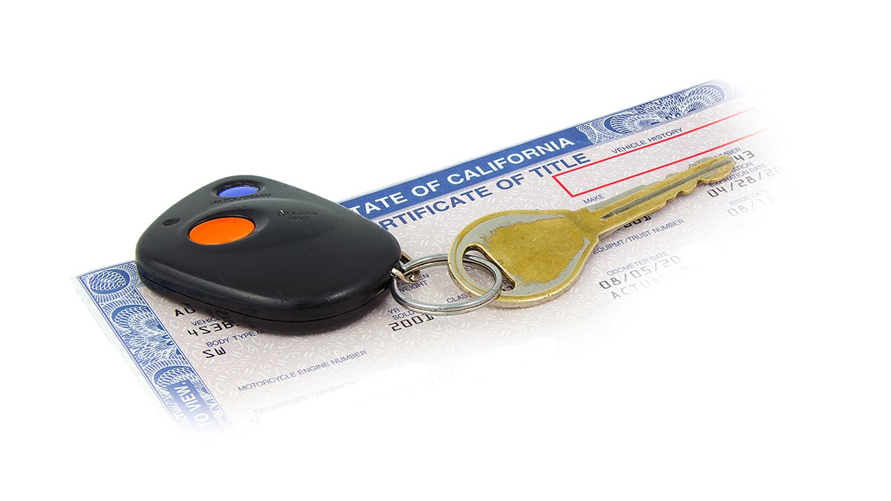 A key fob and car key sit on top of the corner of a car title issued in the state of California