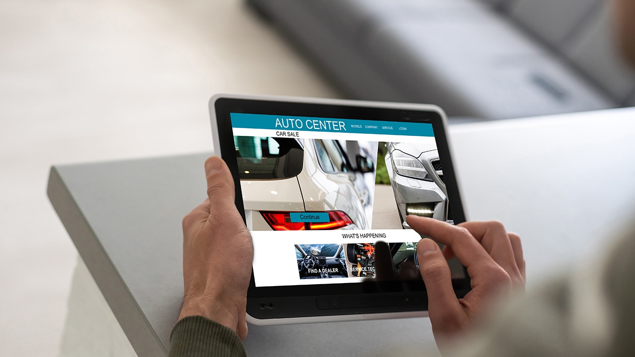 A person's hand touches a tablet screen with car sale information on it