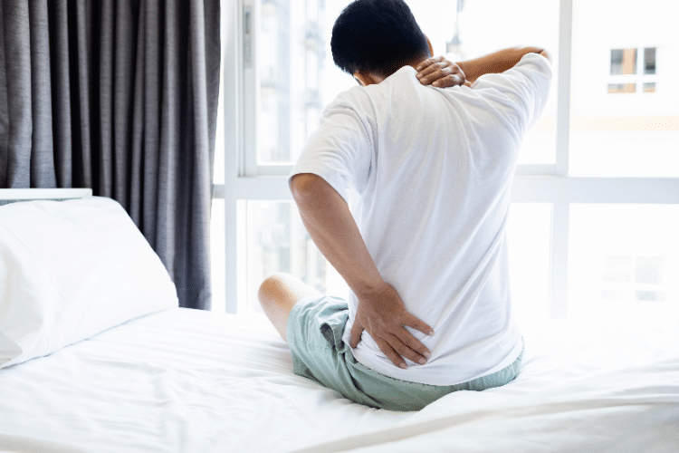 Man grabbing back in pain on bed