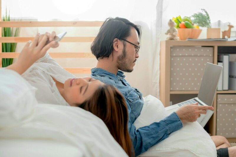 man and woman research mattresses online while relaxing on their bed