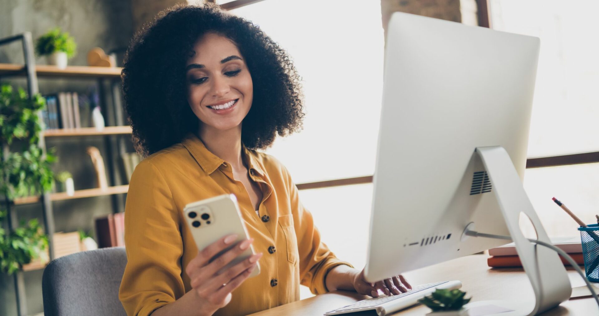 woman looking at phone with computer in front of her