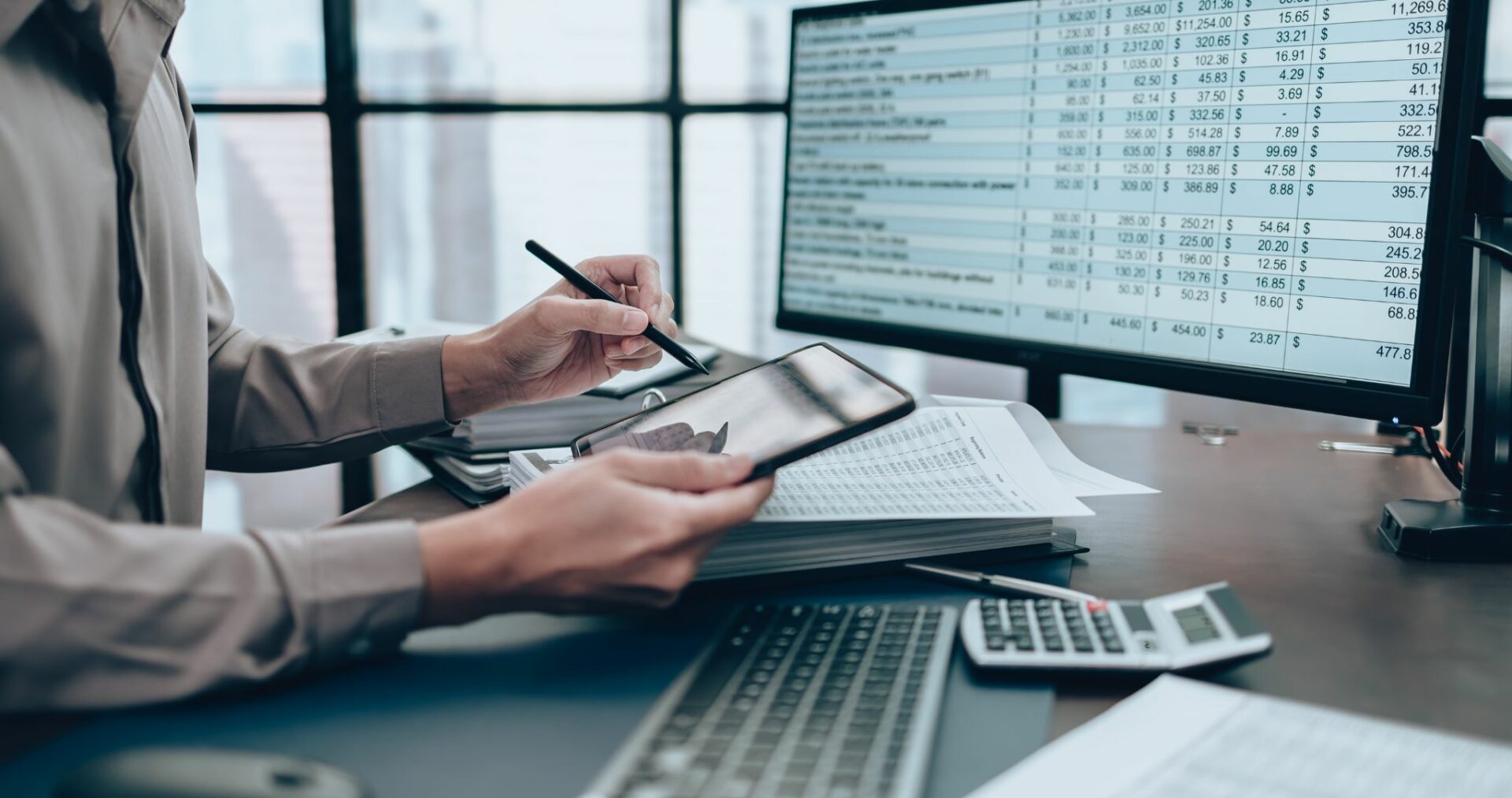 A person using a pen and notepad in front of a computer and calculator