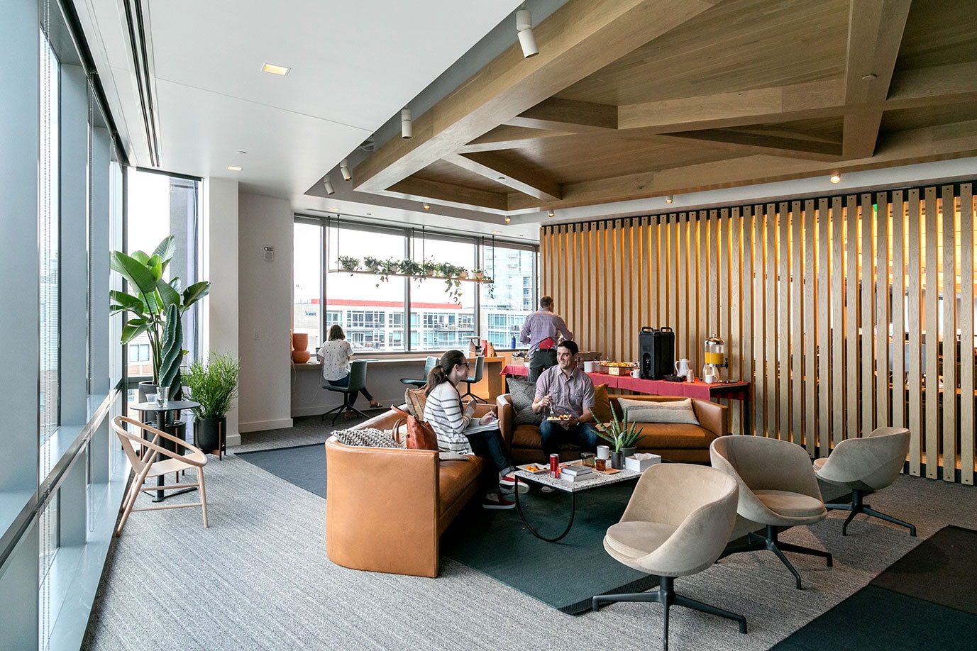 大きな窓と西海岸スタイルの木造建築が特徴的な開放的なオフィス空間。快適そうなソファで 2 人の従業員が休憩している。