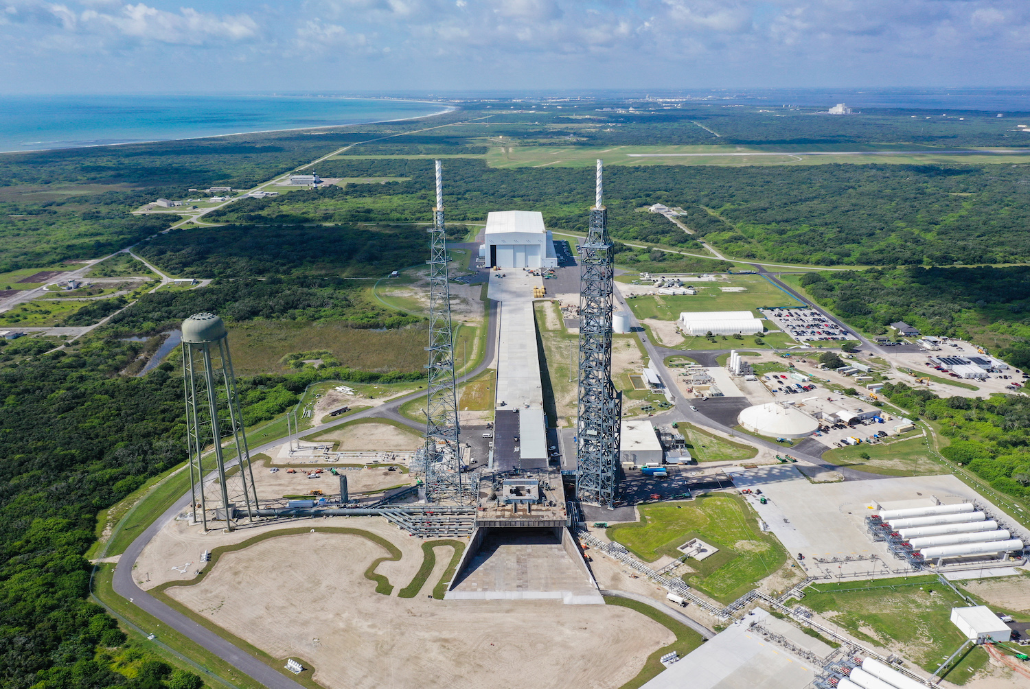 An aerial view of Launch Complex 36, located on the coast of Cape Canaveral, where New Glenn will launch. Two lightning towers, a large white building, and a water tower are in view.