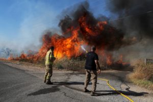 An Israeli firefighter and a man from the immediate responders team work to take control over a fire on the Israeli side o...