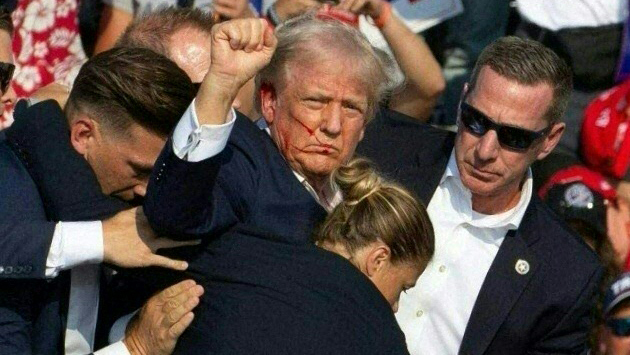 Donald Trump holds up his fist with his face splattered in blood as Secret Service agents swarm him at a campaign rally.