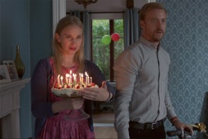 A woman and a man walk in with a lit birthday cake.