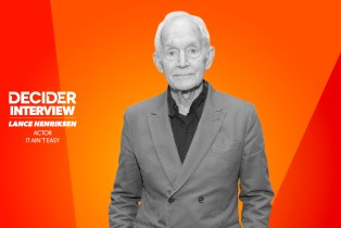 LANCE HENRIKSEN in black and white in front of a bright orange background