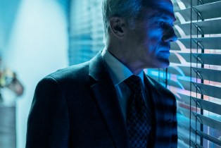 'The Consultant's Christoph Waltz as Regus Patoff peering out blinds in a dark room