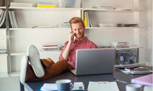 Person with feet up at desk while on the phone looking at computer.