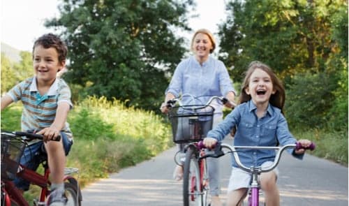 Family smiling on bikes in wooded path.