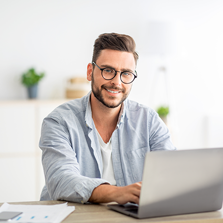 A man working on a laptop and smiling in front of the camera.