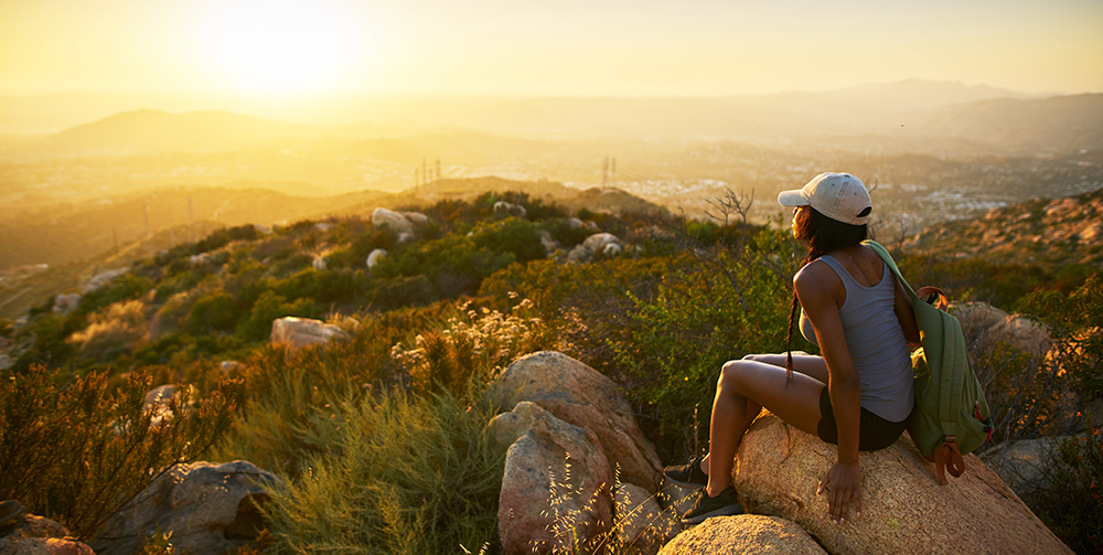 Woman sitting on a rock overlooking a valley at sunset.