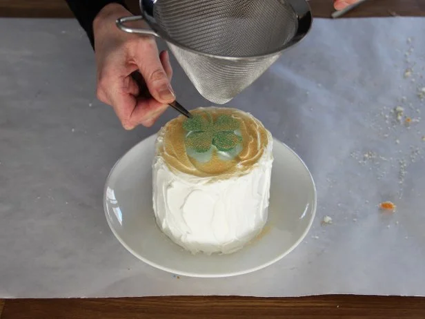 Pour the sanding sugar into a fine mesh sieve. Then, holding the paper template over the center of the cake, shake the sieve gently to sprinkle sugar over the top of the cake.