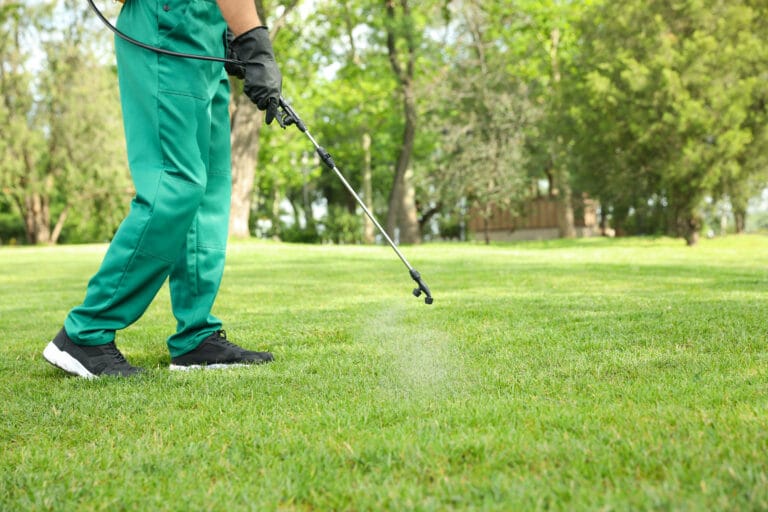 Worker in green exterminator gear spraying pesticide into the grass