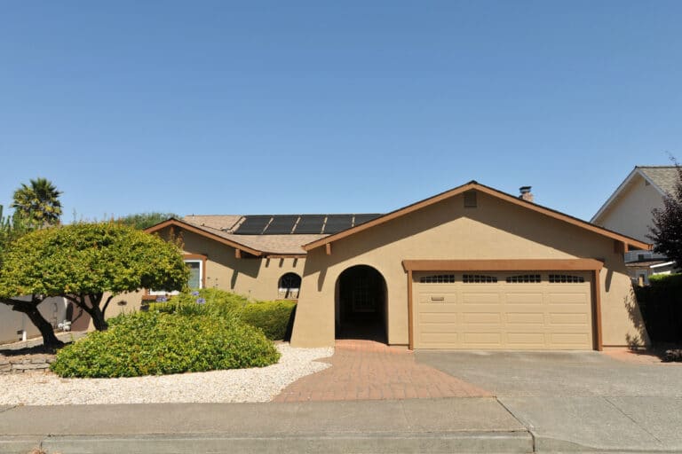 A neutral colored California home with desert landscaping and solar panels on the roof.