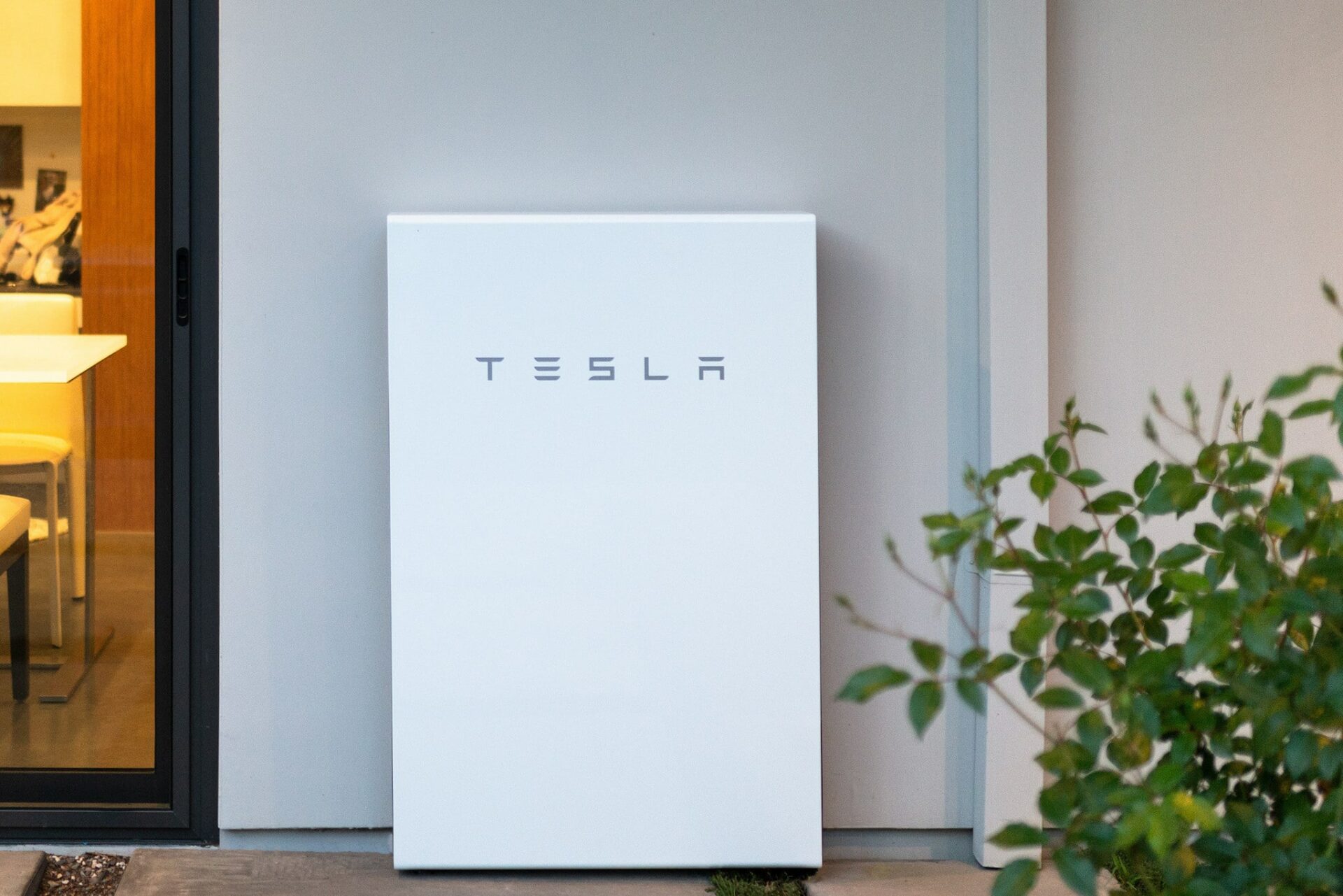 Tesla powerwall against the side of a suburban home.