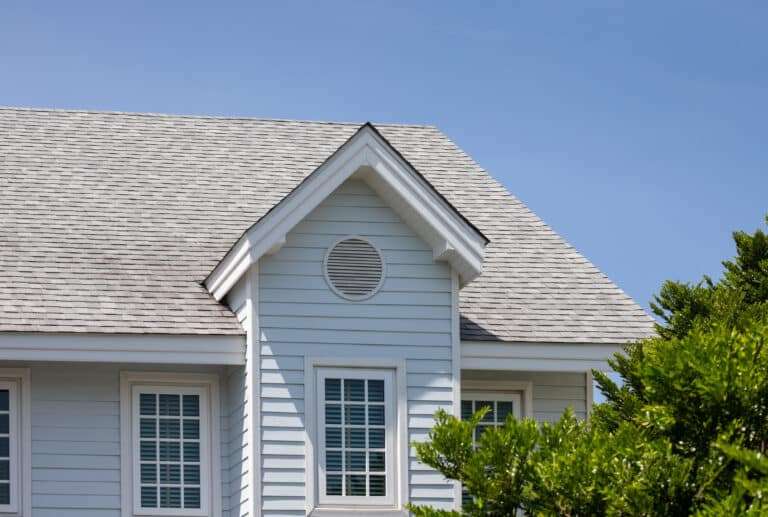 Roof shingles with garret house on top of the house among a lot of trees. dark asphalt tiles on the roof background