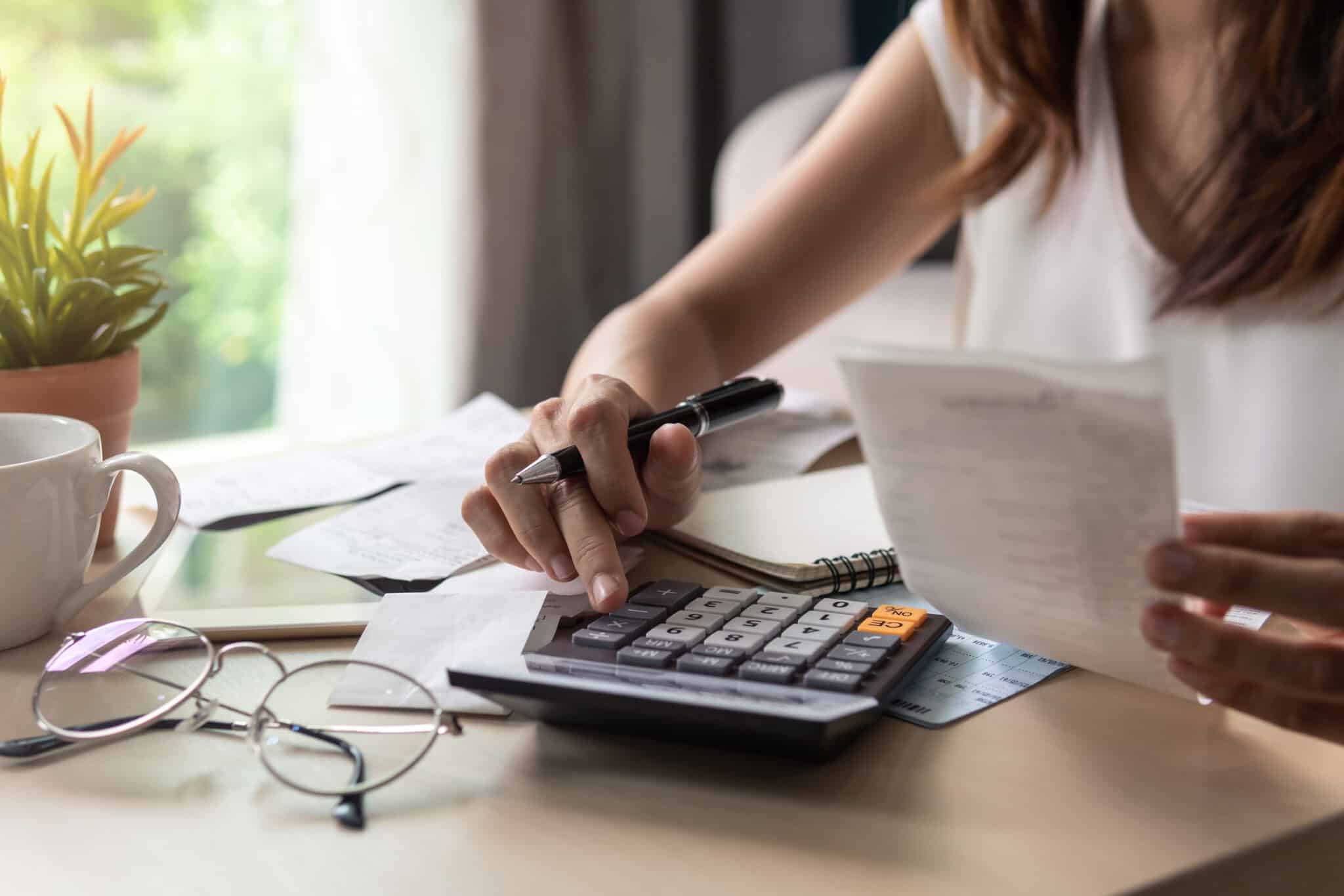 Young woman checking bills, taxes, bank account balance and calculating expenses in the living room at home