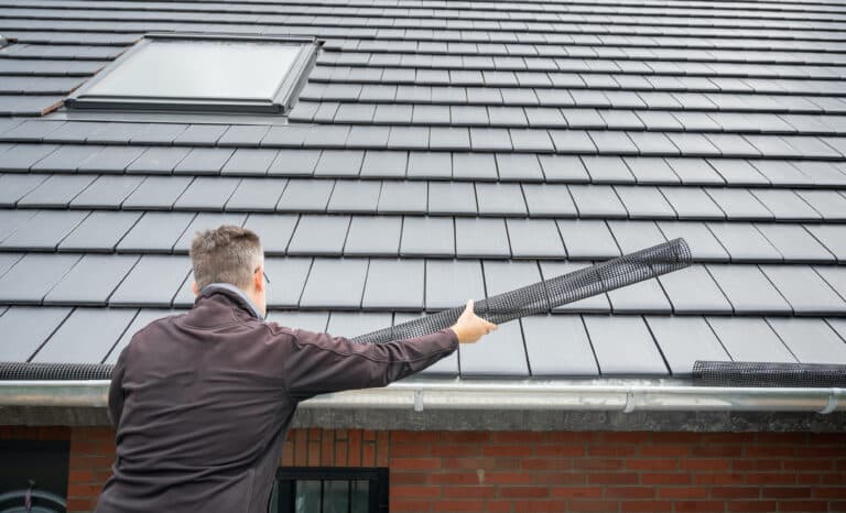 Man puts a gutter mesh to the rain gutter to protect the gutter from leaves.