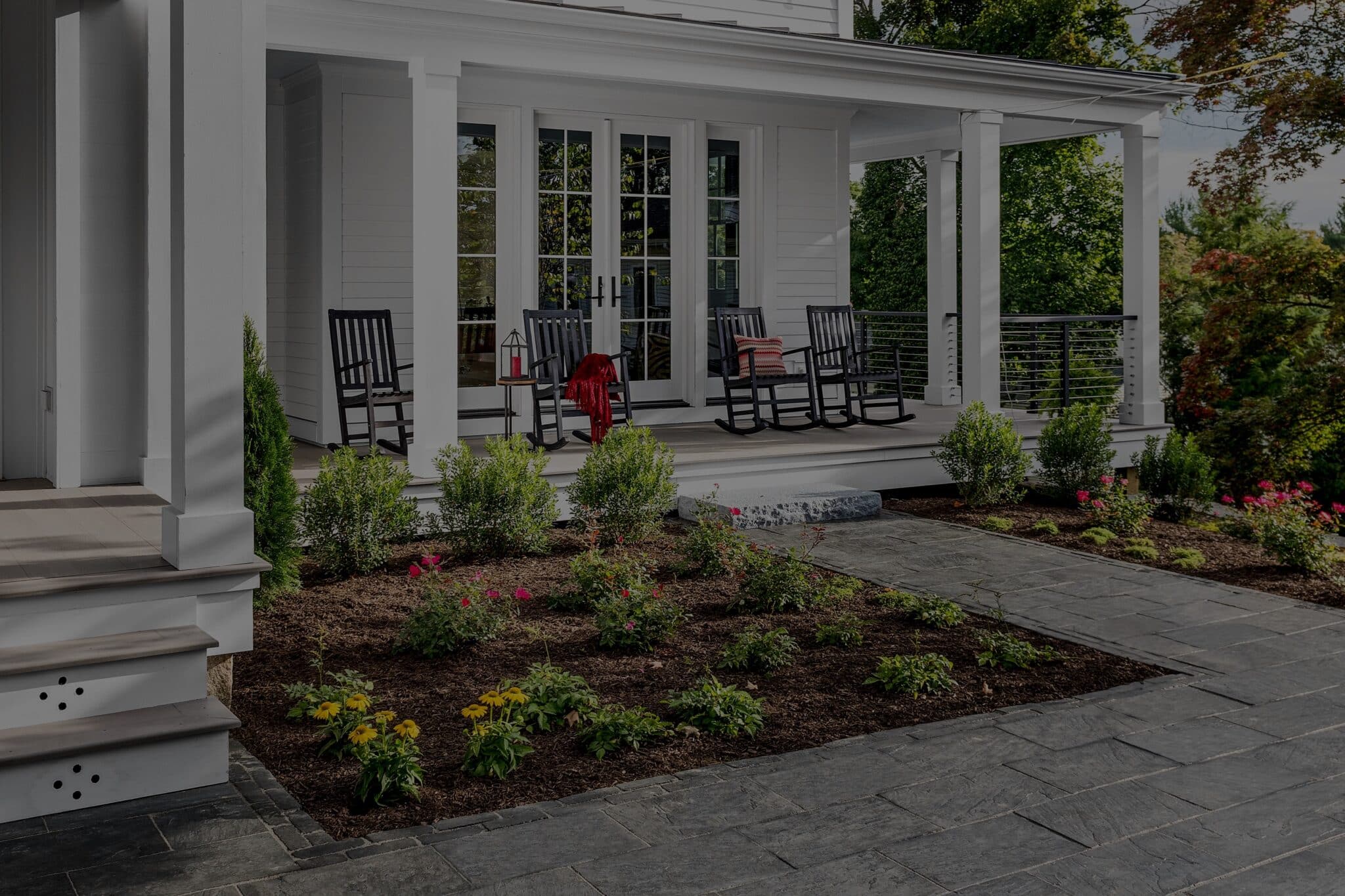 the front porch of a house with landscaping in front of it, including bushes and flowers surrounded by mulch
