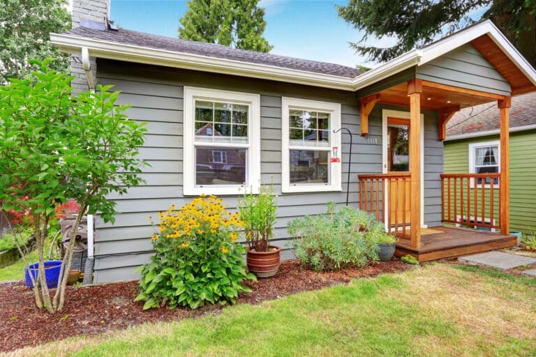 Exterior of a beautiful older one-bedroom home with shrubs and greenery out front