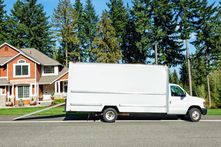 Photo of a plain white moving truck parked on the street in front of a house.