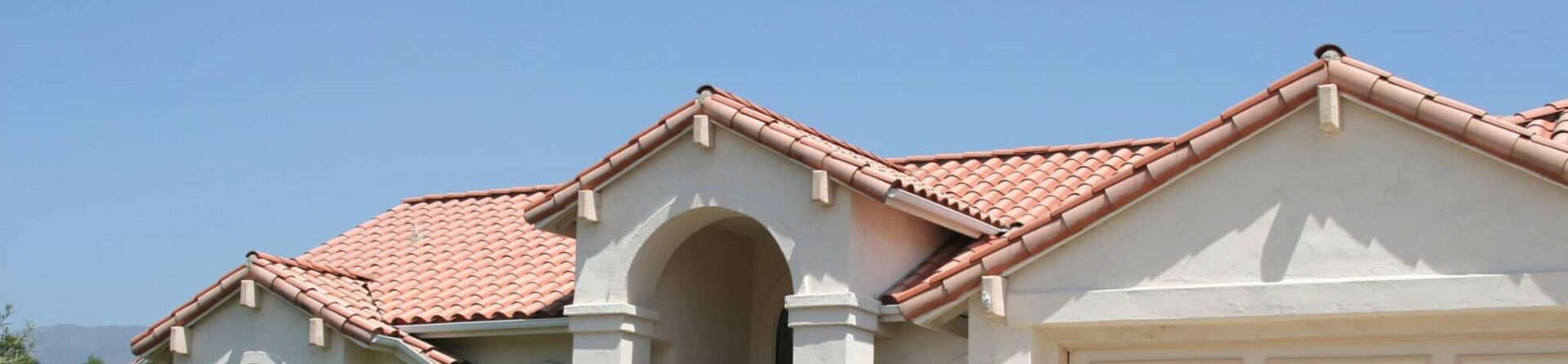 Red clay tile home with landscaping and large driveway on a sunny day.