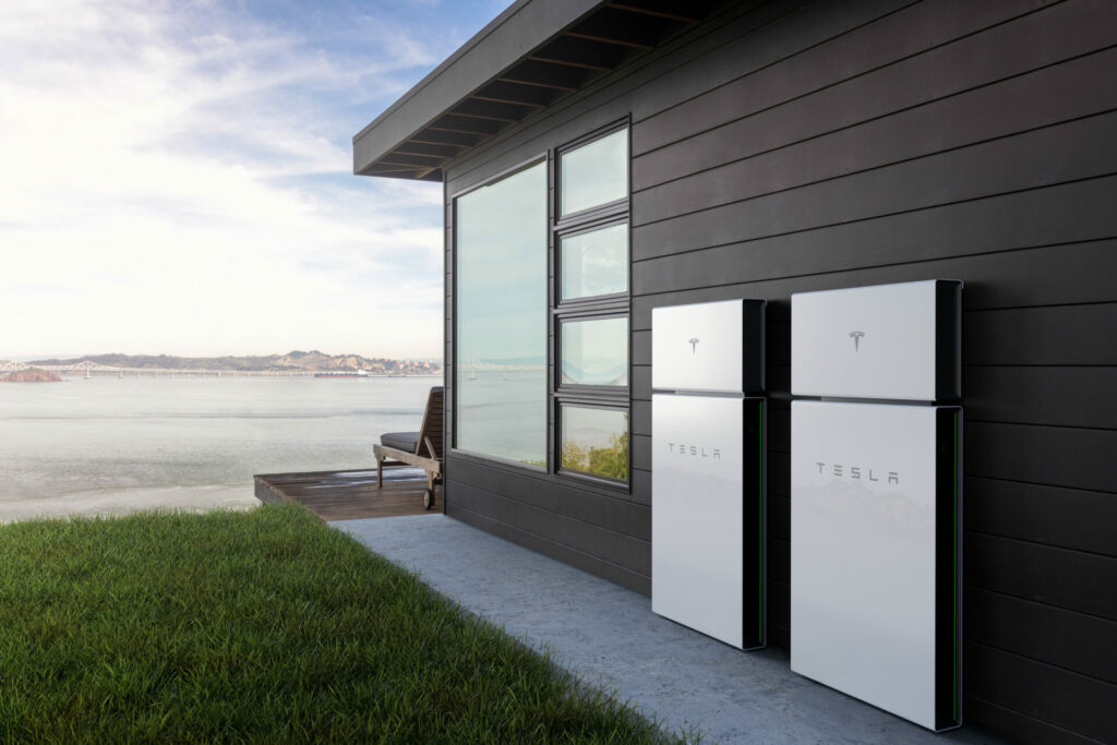 Modern house overlooking a lake with two Tesla Powerwalls on the side of the house.