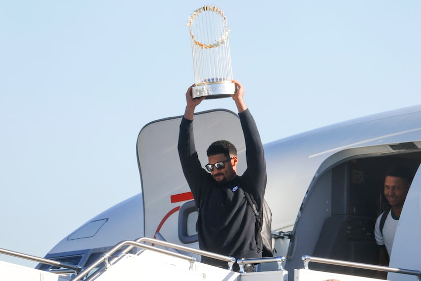 Texas Rangers' Marcus Semien hoists the Commissioner's Trophy next to pitcher José Leclerc...