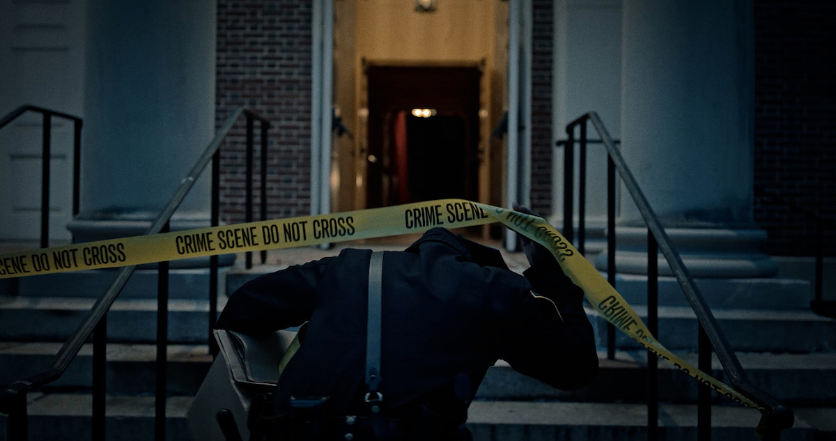 A police officer pulls up crime scene tape.