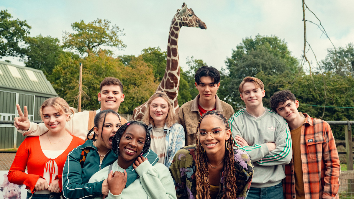 The cast of 'Heartstopper' poses in front of a giraffe at a zoo in Season 3.